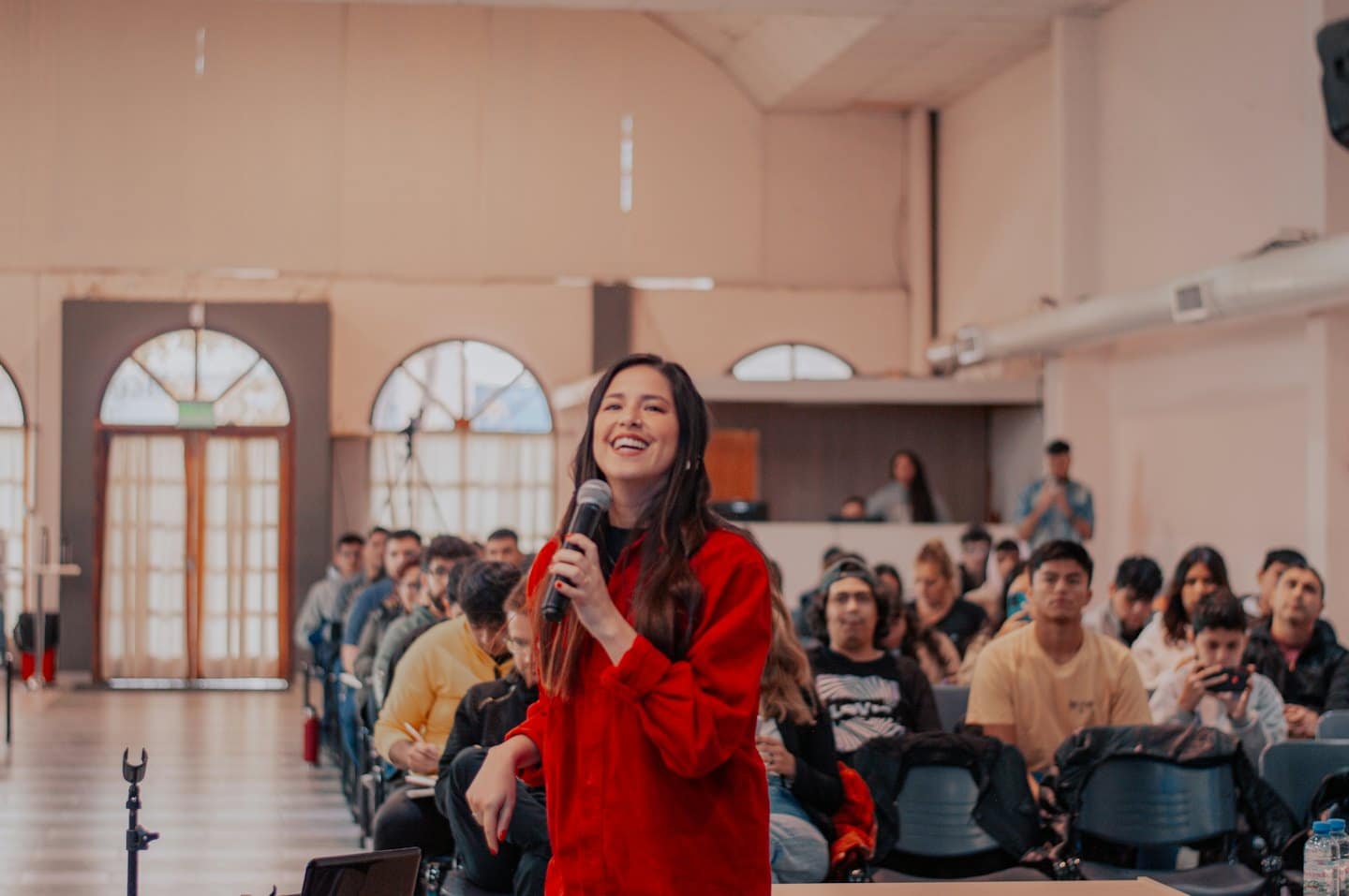 Una donna parla al microfono a un pubblico seduto in una sala.