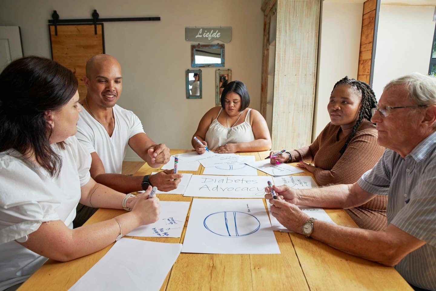 Adulti diversi collaborano attorno a un tavolo con documenti su 'Advocacy per il Diabete'.