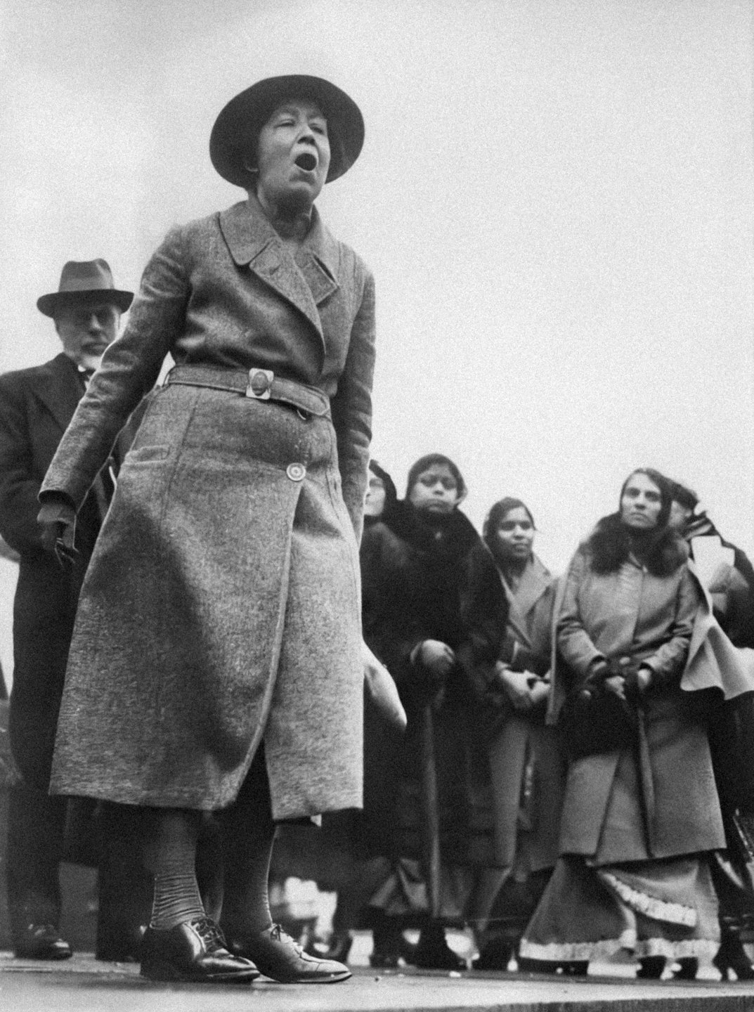 Una donna parla con passione a una folla durante una protesta all'aperto.